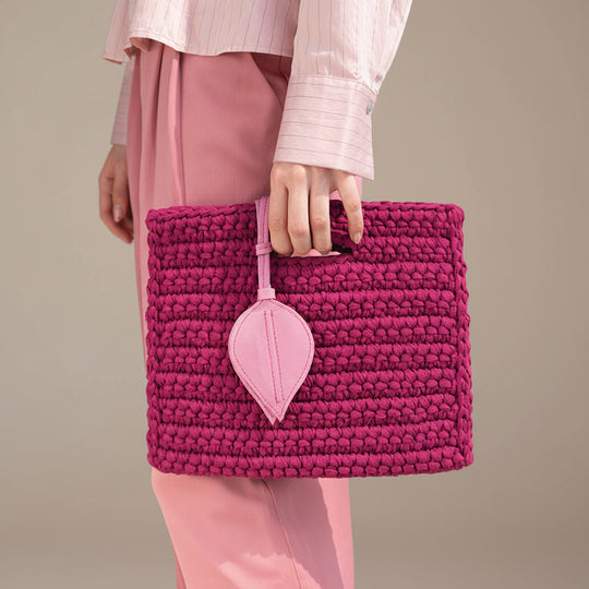 Person holding a pink woven handbag with a heart-shaped tag against a neutral background